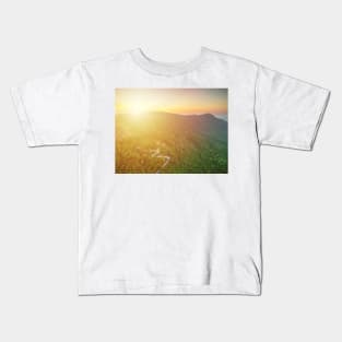 Aerial view of curvy mountain road through a jungle ay sunset Kids T-Shirt